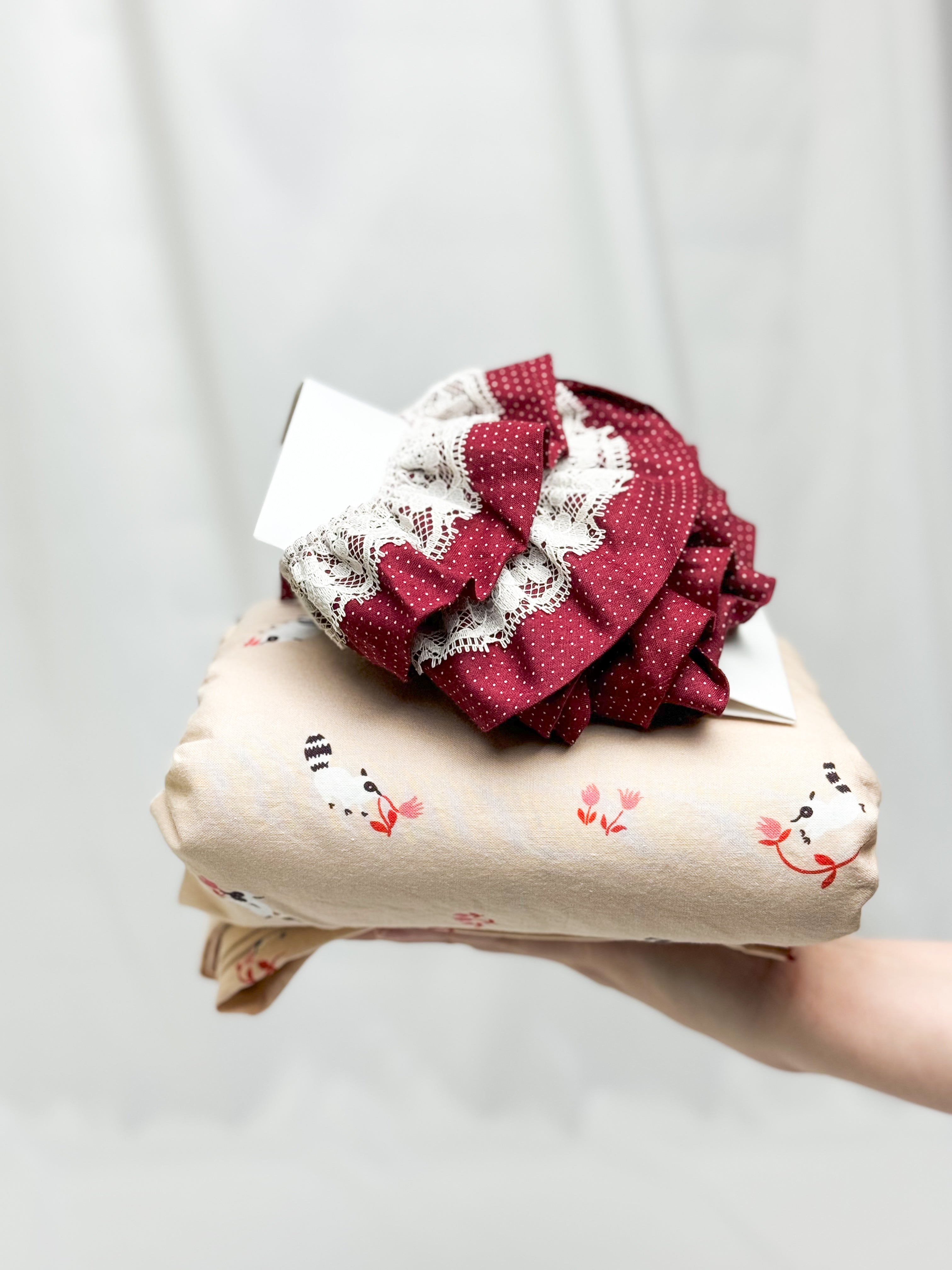 Hand holding a folded fabric item with a decorative red ruffled top against a plain background